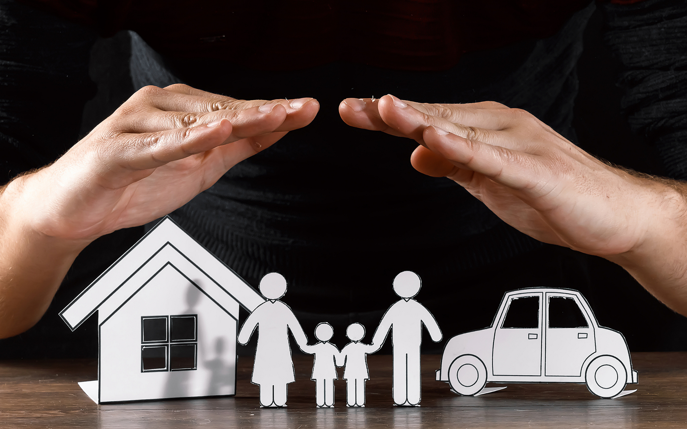 person's hands protecting paper cutouts of family, house, and car